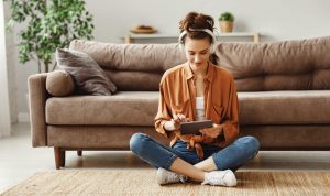 Vrouw met koptelefoon op zit in de woonkamer met tablet in handen