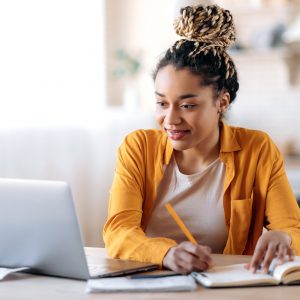 Vrouw zit met laptop en schrift aan tafel te studeren of te werken