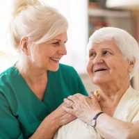 Cliënt met oudere verpleegkundige die na haar pensioen is blijven doorwerken in de zorg