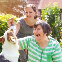 Begeleider en cliënt met een verstandelijke beperking in de tuin met hond